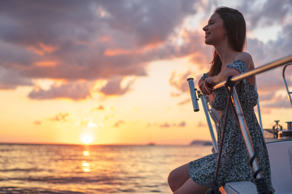 Young attractive woman sitting on the deck of the yacht and enjoying sunset